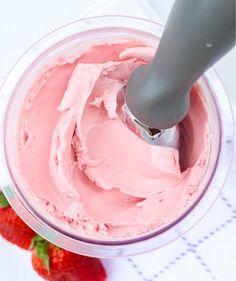 a bowl filled with pink frosting next to strawberries