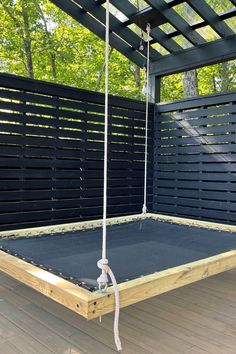 a wooden swing suspended from the ceiling in front of a black privacy fence and wood flooring