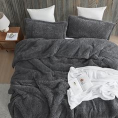 an unmade bed with white pillows and blankets on it, next to a wooden wall