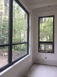 an empty room with two windows and no curtains on the outside, in front of trees