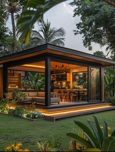 a small house is lit up at night in the yard with plants and trees around it