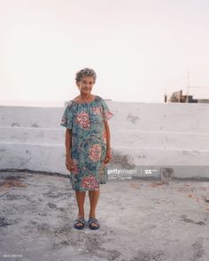 an older woman standing in front of a white wall and looking at the camera with her hands on her hips