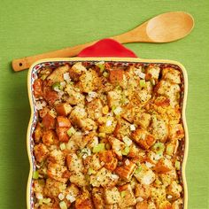 a casserole dish filled with stuffing and vegetables next to a wooden spatula