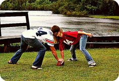 two people are bending over to pick up something from the grass near a body of water