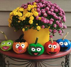 painted pumpkins with faces on them sitting in front of a potted plant and flowers