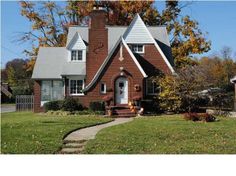 a red brick house with a white door and windows in the front yard on a fall day