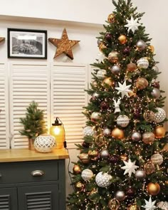 a decorated christmas tree sitting in front of a window next to a dresser and framed pictures