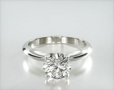 a white gold engagement ring with a round brilliant cut diamond in the center, on a plain surface