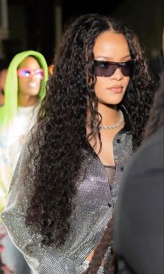 a woman with long curly hair wearing sunglasses and standing next to another woman in front of her