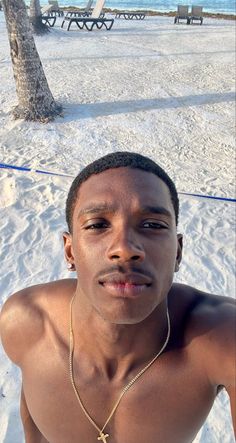 a man with no shirt on sitting in the snow next to a tree and beach