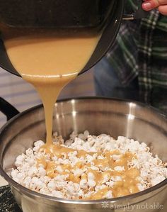 a person pouring caramel sauce into a pot filled with white and brown popcorn kernels