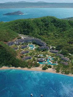 an aerial view of the resort surrounded by trees and blue water with boats in it