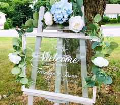 a welcome sign sitting on top of a wooden easel with flowers and greenery