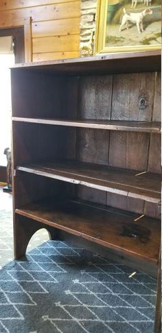 an old wooden bookcase sitting on top of a blue carpeted floor next to a painting