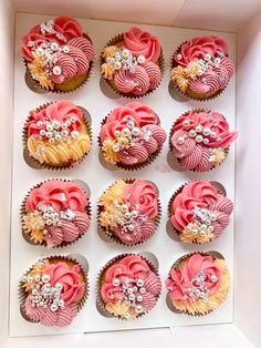 twelve cupcakes in a box decorated with pink, yellow and white frosting