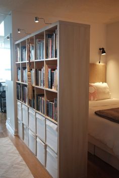 a bed sitting next to a tall book shelf filled with books on top of a hard wood floor