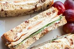 a sandwich cut in half sitting on top of a plate next to grapes and plums