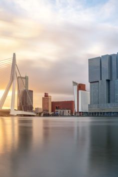 the sun is setting behind some tall buildings on the water's edge in front of a body of water