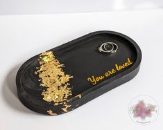 a black tray with gold flakes on it that says you are loved and has a ring in the middle