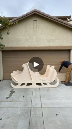 a man working on a wooden sled in front of a house with garage doors