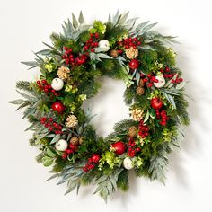 a christmas wreath hanging on the wall with pine cones, berries and other greenery