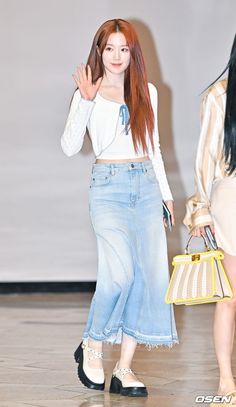 the girl is walking down the runway with her hand up in the air while wearing a white top and blue skirt