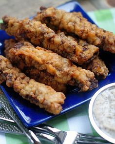 a blue plate topped with chicken wings next to a bowl of ranch dressing and silverware