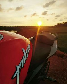 the back end of a red motorcycle parked on top of a dirt road next to a body of water