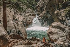 two people sitting on rocks in front of a waterfall