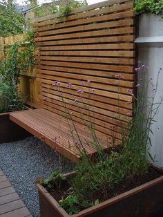 a wooden bench sitting in the middle of a garden next to a wall with plants growing on it