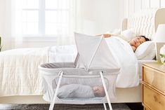 a woman laying in bed next to a baby bassinet and sleeping on top of it