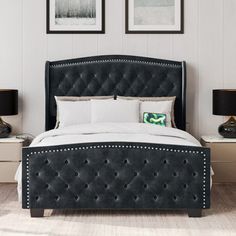 a bed with black headboard and white sheets in a room next to two pictures on the wall