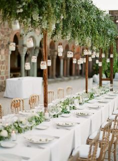 a long table with white linens and greenery is set up for an outdoor dinner