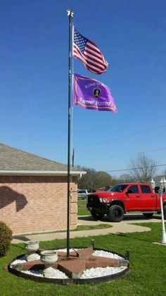 an american flag flying in the wind next to a purple and white flag on a pole