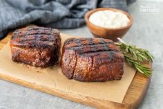 two steaks sitting on top of a wooden cutting board