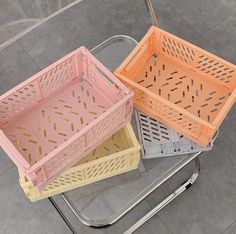 three plastic crates sitting on top of a metal table next to each other, one yellow and one pink