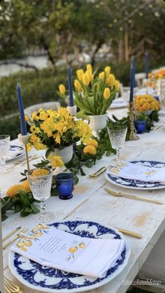 a long table with yellow flowers and blue plates on it, along with place settings