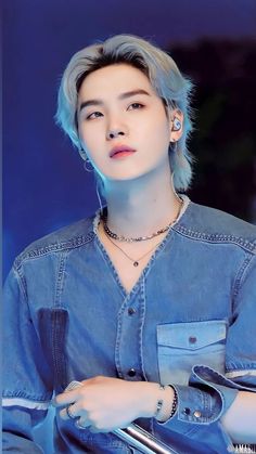 the young man with blue hair is wearing a denim shirt and silver earrings