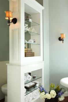 a bathroom with a white toilet sitting next to a shelf filled with towels and flowers