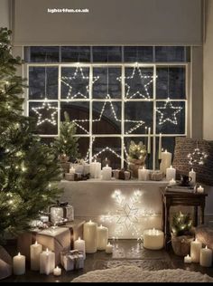 a christmas tree with lit candles in front of a window and presents under the windowsill