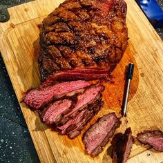 a large piece of meat is on a cutting board next to a knife and fork