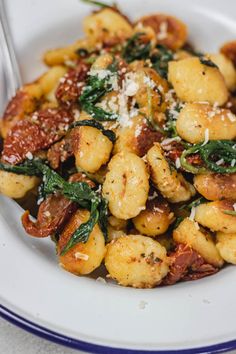 a white plate topped with pasta and spinach covered in sauce next to a fork