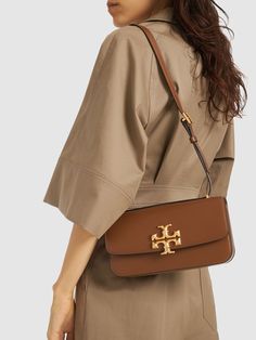 Height: 12.5cm Width: 23.5cm Depth: 6.2cm. Leather strap. Front flap with magnetic closure. Front metal logo detail. One internal zip pocket Tory Burch Eleanor Bag, Tory Burch Bag, Purple Bags, Brown Bags, Metal Logo, Metallic Logo, Women's Bags, Magnetic Closure, Cloth Bags