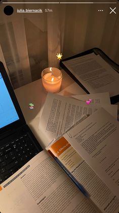 an open laptop computer sitting on top of a desk next to papers and a lit candle