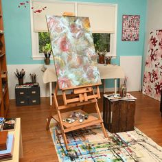 an artist's easel in front of a window with blue walls and wooden floors