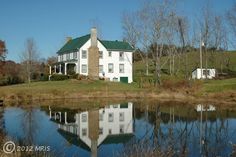 a large white house sitting on top of a lush green hillside next to a lake