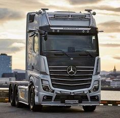 the front end of a mercedes benz semi truck parked in front of a body of water