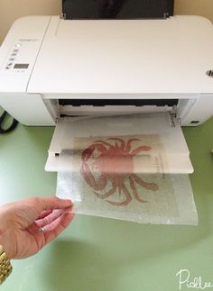 a person is holding a piece of paper in front of a printer that has an octopus on it