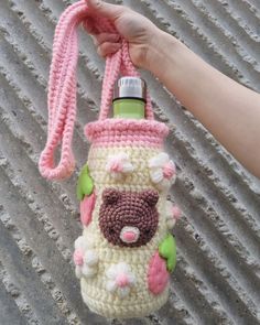 a crocheted water bottle holder with a pink handle is held up by a woman's hand