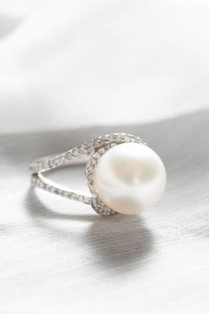 a white pearl and diamond ring sitting on top of a silver cloth covered tablecloth